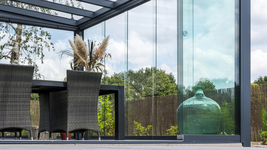 Modern outdoor patio with glass walls, chairs, and a decorative vase.