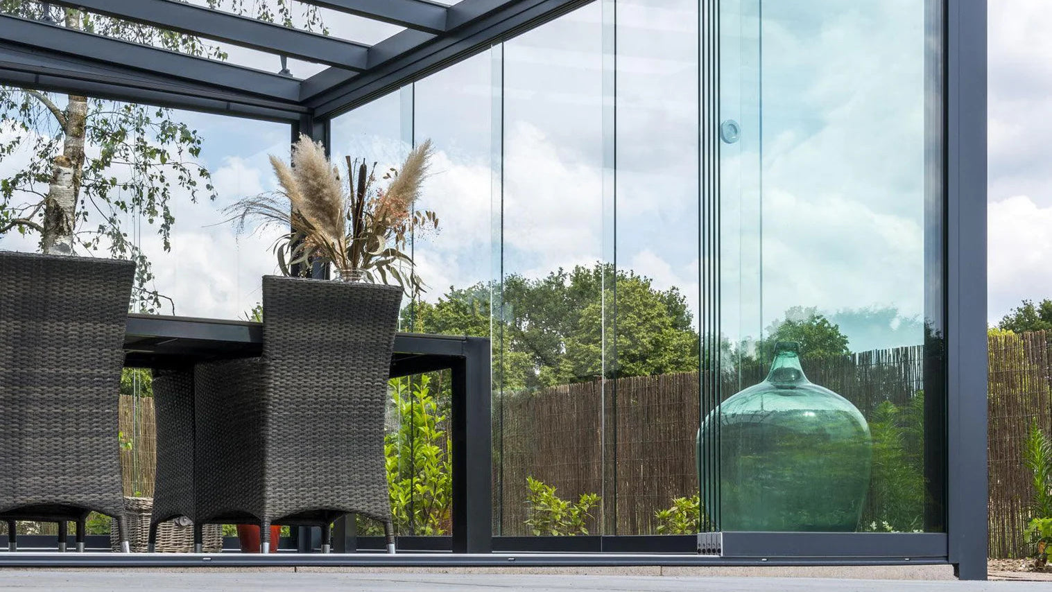 Modern outdoor patio with glass walls, chairs, and a decorative vase.