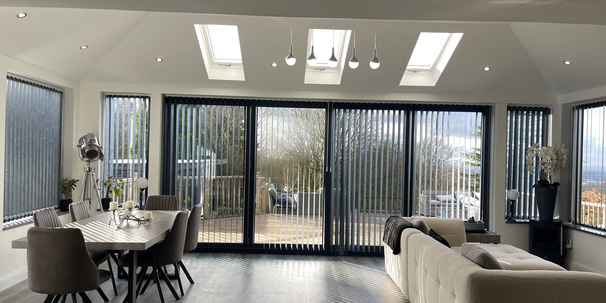 A converted conservatory used as a dining and living room, with a plastered vaulted ceiling, three roof windows and anthracite bi-fold doors onto a deck